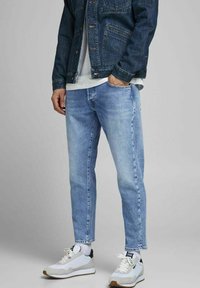 Ljusblå denimjeans med en avslappnad passform, kombinerat med en vit t-shirt och en mörkblå denimjacka. Vita och grå sportskor.