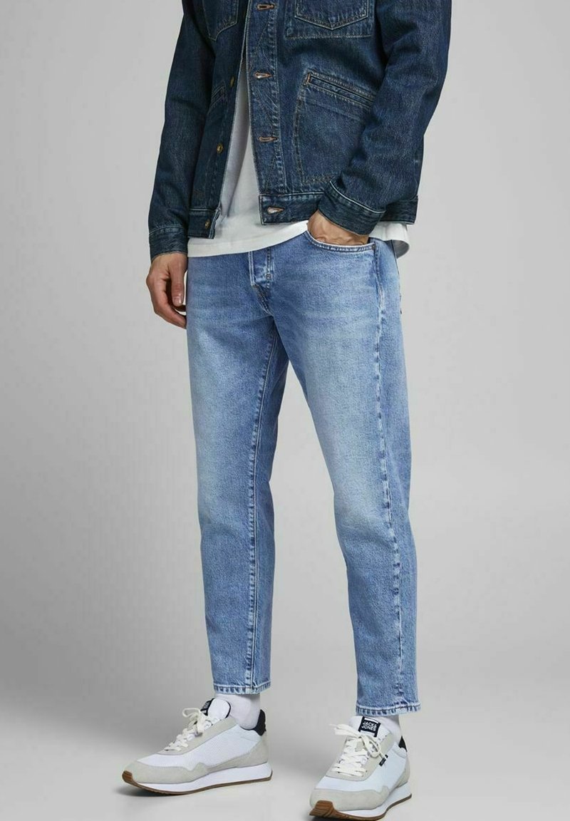 Ljusblå denimjeans med en avslappnad passform, kombinerat med en vit t-shirt och en mörkblå denimjacka. Vita och grå sportskor.