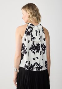 Must mustrilineeritud musta lillemustriga halter-top, kergetest materjalidest, millel on pleedid ja kaeluses pael, koos musta pleeritud seelikuga.