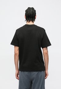 Czarny bawełniany t-shirt z krótkimi rękawami, okrągłym dekoltem i luźnym krojem. Widoczne przeszycia na dole oraz gładka faktura.