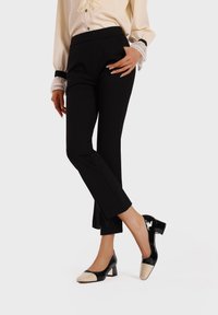 Pantaloni tailored neri con una vestibilità slim e spacchi laterali, abbinati a tacchi in vernice neri e beige con design a blocco.