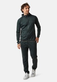 Dark grey athletic hoodie and matching pants, made of textured fabric, featuring a full zip, hood, and side pockets. Accented with white sneakers.