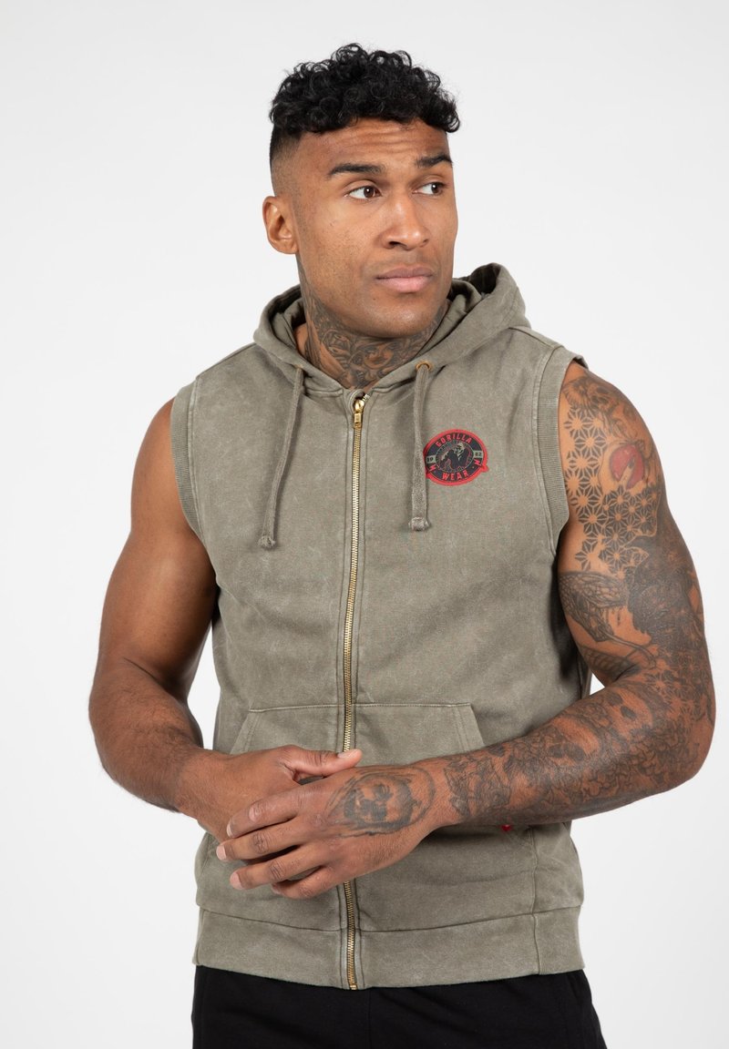 Mouwloze olijfgroene hoodie met rits en een capuchon met koord, voorzakken en een cirkelvormig rood logo op de borst. Zachte, gestructureerde stof.