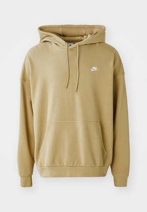 Beżowa bluza z kapturem Nike z kieszenią z przodu, kapturem ze sznurkiem, długimi rękawami i małym białym logo Nike na piersi, pokazana na jednolitym tle.