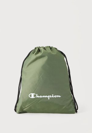 Sac à cordon vert avec cordons noirs et logo blanc Champion à l'avant sur un fond clair uni.