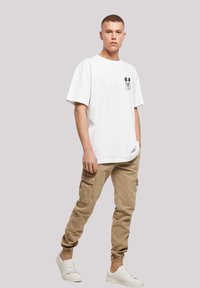 Hvid bomulds t-shirt med et sort Mickey Mouse grafisk motif på brystet, parret med beige cargo bukser og hvide sneakers.