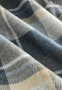 Soft fabric with a plaid pattern in blue, gray, white, and beige, showing folds and textured fibers.