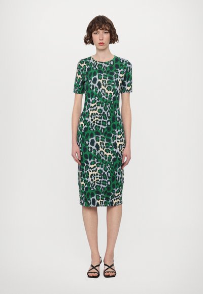 Robe verte à imprimé léopard avec une silhouette mi-genou, des manches courtes, un col rond et un tissu texturé. Portée avec des sandales noires à lanières.