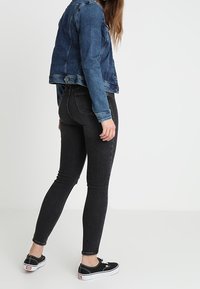 Mörk tvätt av smala jeans med hög midja och subtila slitningar. Kombinerat med en blå denimjacka och svarta kanvas sneakers.