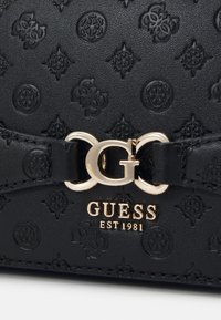 Borsa a mano in pelle nera con effetto goffrato, dotata di una chiusura a logo dorato e del nome del marchio "GUESS EST 1981." Motivo testurizzato con un design intricato.