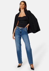 Svart strapless topp, denimjeans och svarta högklackade skor. Modellen har på sig en oversized svart kavaj som hänger över ena axeln.