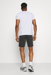 T-shirt en coton gris, shorts en denim noir et baskets grises avec des accents verts. Manches courtes, coupe décontractée, ourlet roulé sur les shorts. Fond neutre.
