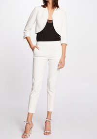 Vit kort jacka över en svart tanktopp, i kombination med vita skräddarsydda byxor. Silverfärgade sandaler med hög klack och remmar fulländar looken.