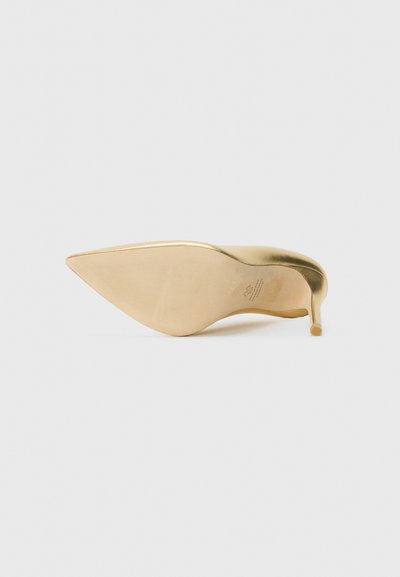 Chaussure à talons aiguilles dorée vue du dessous avec un talon slim sur un fond blanc.