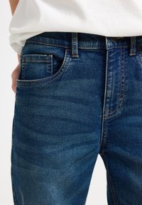 Tmavě modré džíny z denimu s jemným vypáleným vzorem, s kontrastním šitím, bočními kapsami a standardním pasem.