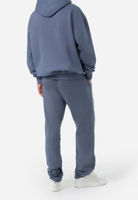 Sudadera con capucha y pantalones jogger a juego en un tejido suave y texturizado, con un color azul apagado. Incluye bolsillos laterales y puños acanalados.