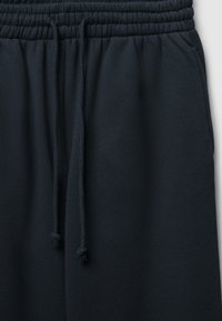 Pantaloni tuta blu navy con cintura elastica e cordino regolabile. Il tessuto sembra morbido con una superficie liscia e dettagli di cucitura minimi.