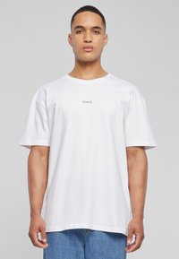 Hvid bomulds t-shirt med en afslappet pasform, rund halsudskæring og korte ærmer, med ordet "loved." trykt centralt i lys lilla.