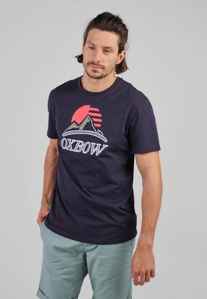 Camiseta de algodón de cuello redondo en azul marino con un gráfico de montaña y el texto "OXBOW" en blanco y acentos coloridos. Mangas cortas y corte relajado.