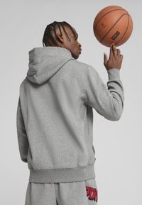 Grijze hoodie met een grote kap en textuurstof, met geribbelde mouwen en onderrand. Een basketball is in balans op de vinger van het model.