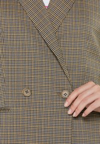 Brown and blue checkered blazer with a double-breasted design, featuring large brown buttons and a smooth fabric texture.