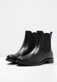Black leather Chelsea boots with elastic side panels, rounded toe, and low stacked heel. Smooth texture and minimalistic design.