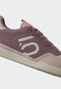 Sneaker viola e beige con tomaia in suede e tessuto, caratterizzate da un logo prominente, lacci e suola in gomma.