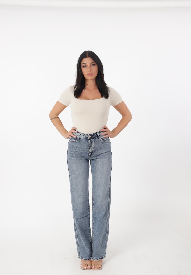 Top ajustado color beige claro con escote cuadrado, combinado con vaqueros de pierna recta de talle alto en azul. Sandalias transparentes completan el conjunto.