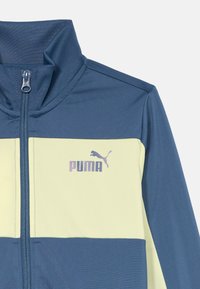 Blå och cremefärgad Puma-jacka med dragkedja framtill och hög krage, som har Puma-logotypen på vänster bröst.