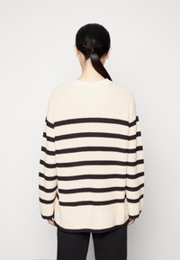 Dzianinowy sweter z poziomymi czarnymi i kremowymi paskami, o prążkowanej fakturze, długich rękawach i okrągłym dekolcie, widziany od tyłu.