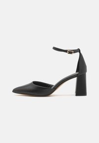 Black high-heeled shoe with a pointed toe, textured ankle strap, and a square block heel. Made of smooth leather.