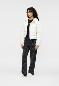 Λευκό μπουφάν τύπου puffer, σχέδιο croppped, φερμουάρ μπροστά, μακριά μανίκια. Μαύρο παντελόνι με γεωμετρικό σχέδιο. Λευκά αθλητικά παπούτσια, μαύρο t-shirt.