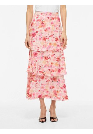 Kvinde iført en pink blomsterprintet flæset midi-nederdel og sorte åbne hæle, der står mod en hvid baggrund.