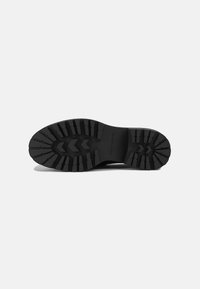 Sole in gomma nera con un battistrada testurizzato e decorato che presenta scanalature a zigzag e un logo circolare al centro.