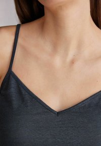 Grijze tanktop met dunne bandjes en een V-hals. De stof lijkt zacht met een lichte glans en subtiele textuur. Eenvoudig, minimalistisch ontwerp.