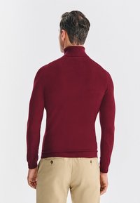 Bordowy sweter z golfem o dopasowanym kroju, z dzianiny o teksturze, z prążkowanym kołnierzem, zestawiony z jasnymi spodniami.