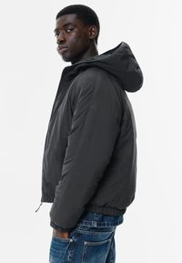 Sort hættetrøje med tekstureret overflade, elastiske manchetter og en forlomme. Bæres med blå denim jeans, der har en afslappet pasform.