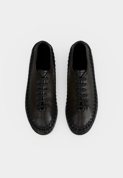 Paire de chaussures en cuir noir à lacets avec des détails tressés le long des bords, vues de dessus sur fond blanc.