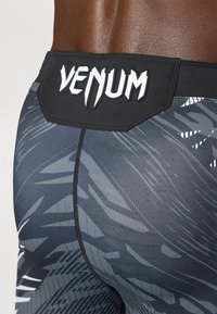 Pantaloni corti compressivi Venum con una vita nera, caratterizzati da un logo bianco e un design grigio scuro con motivi astratti e accenti testurizzati.