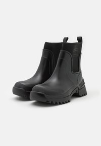 Bottines noires imperméables à la semelle en caoutchouc texturé et panneaux élastiques latéraux ; arbore un logo sur le côté extérieur et des tirettes pour un enfilage facile.