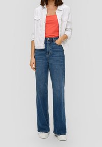 Veste en denim blanche sur un débardeur corail vif, associée à un jean large taille haute bleu et des baskets blanches, créant un look décontracté.