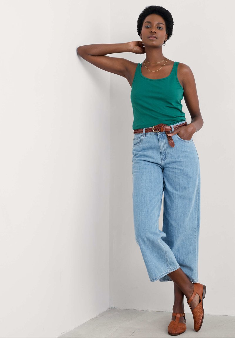 Top verde, jeans azzurri a vita alta, cintura intrecciata marrone e scarpe basse marroni. Design minimalista con una vestibilità comoda.