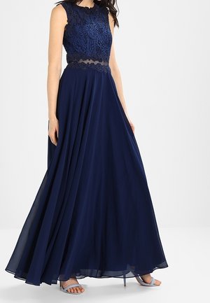 Ærmeløs aftenkjole i marineblå med blonder på overdelen, gennemsigtig taljedetalje, flydende chiffon nederdel, båret med sølvfarvede åbne hæle.