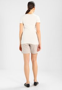 Lehká, přiléhavá bílá tričko spárovaná s béžovými šortkami. Outfitu dominuje jednoduchý design a doplňují ho černé slip-on boty.
