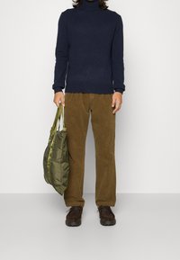 Námořnický rolák, hnědé kordurové kalhoty, tmavě hnědé boty a olivově zelená taška s kontrastními popruhy. Jednoduchý a funkční outfit.