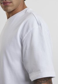 White cotton t-shirt with a relaxed fit, crew neck, and short sleeves; smooth texture with subtle stitching detail at the shoulders.