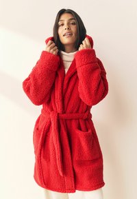 Roter, flauschiger Fleece-Bademantel mit Kapuze, Fronttaschen und einem selbstbindenden Gürtel. Er verfügt über ein strukturiertes, gemütliches Material und ein offenes Design.