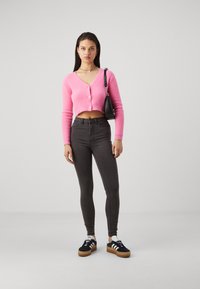 Pink cropped cardigan in textured fabric, gray high-waisted jeans, black sneakers with white accents, and a black handbag.