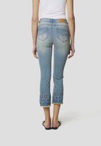 Lichtblauwe denim capri's met geborduurde, gedetailleerde manchetten in blauw, goud en crème. Heeft een taille met een normale hoogte en een rafelige zoom.