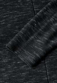 Schwarzer, strukturierten Stoff mit einem marmorierten Muster, versehen mit einem gerippten Bündchen. Das Material wirkt weich und gestrickt mit unterschiedlichen Schattierungen von Schwarz und Grau.